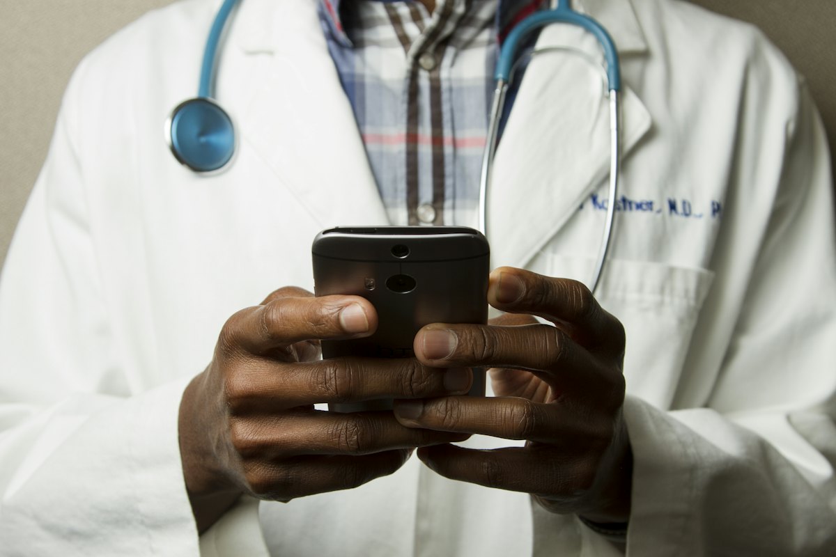 Doctor with a stethoscope reviewing a patient request on a smartphone